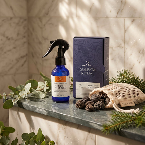 Ignis et Rosa Complete Ritual: the Ignis et Rosa ritual mist beside the Anchor Kit box and a mesh bag of volcanic stones on a marble shower ledge